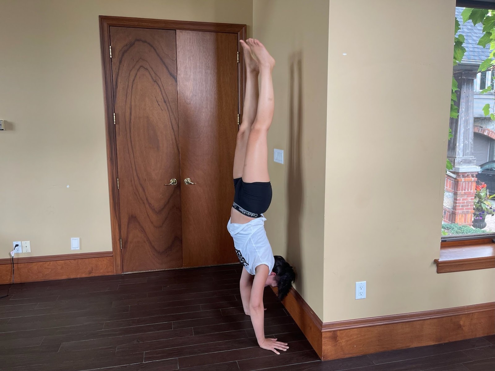 Tarzan does a handstand very near to a wall, her plain white tshirt exposes the ads she worked very hard to get, and she wears black calvin klein men's boxers.